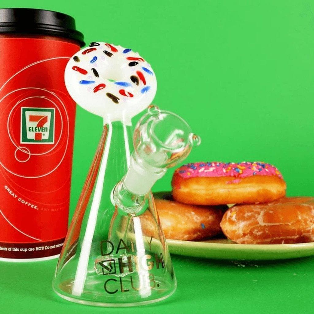 A studio shot features the DHC Originals "Frosted Donut" Bong alongside colorful donuts, showcasing its clear glass construction and playful design.